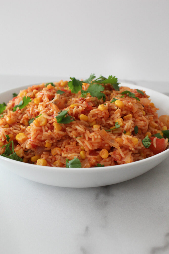 Rice braised in a tomato sauce in a white bowl with vegetables and cilantro.