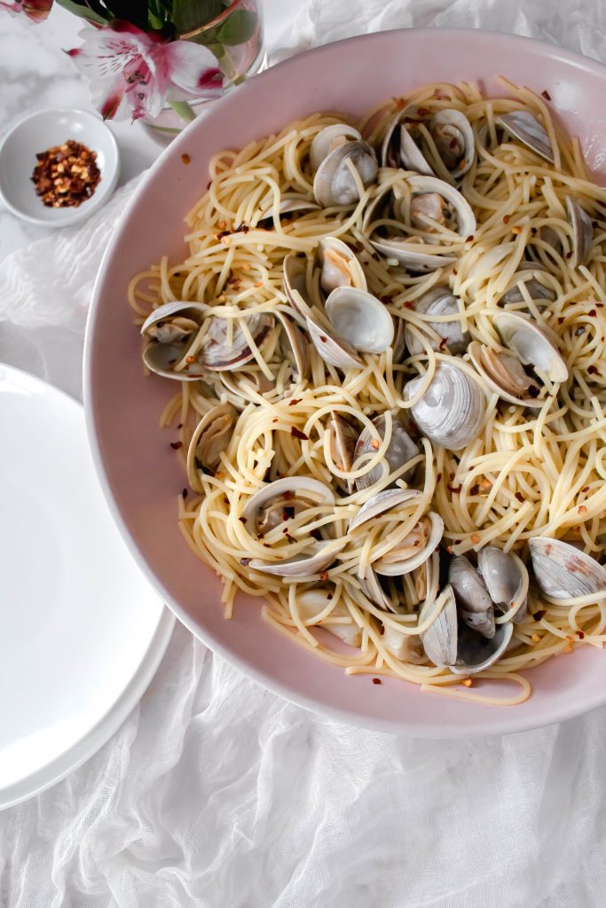 Linguine and clams with red pepper flakes sitting in a pink serving bowl.
