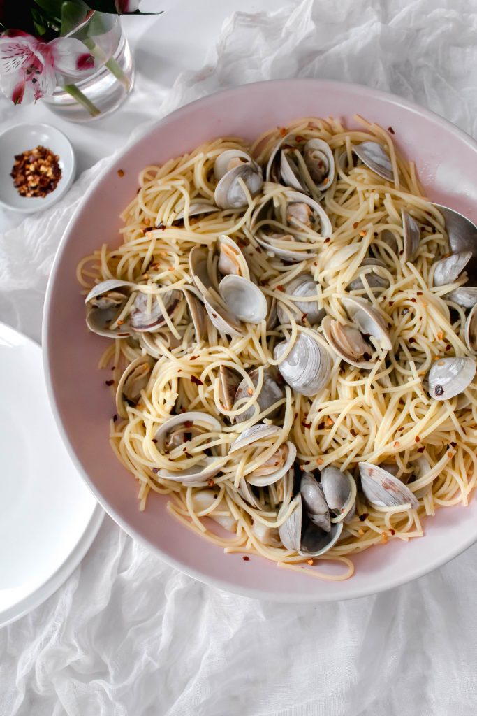 Linguine and clams with red pepper flakes sitting in a pink serving bowl.