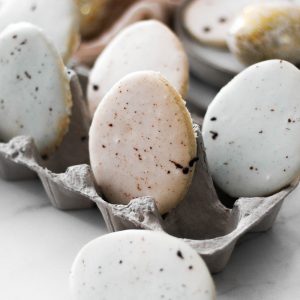 Blue and rose colored egg shaped cookies with speckles sitting in an egg carton.