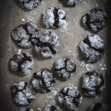 Easy Gluten Free Chocolate Crinkle Cookies laying flat on a cookie tray on brown parchment paper
