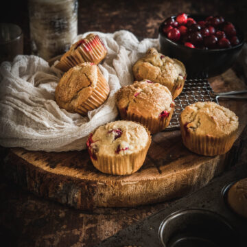 Gluten Free Cranberry Orange Muffins on a wooden slab with a cloth and cranberries