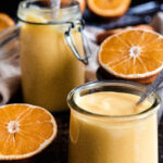Orange curd in two jars surrounded by sliced oranges
