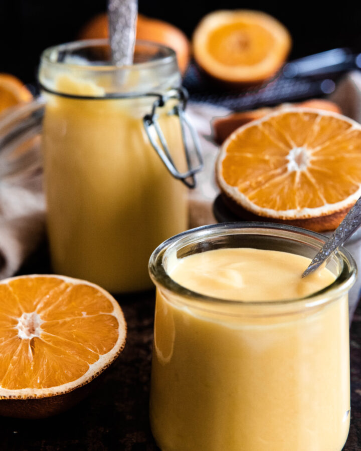 Orange curd in two jars surrounded by sliced oranges
