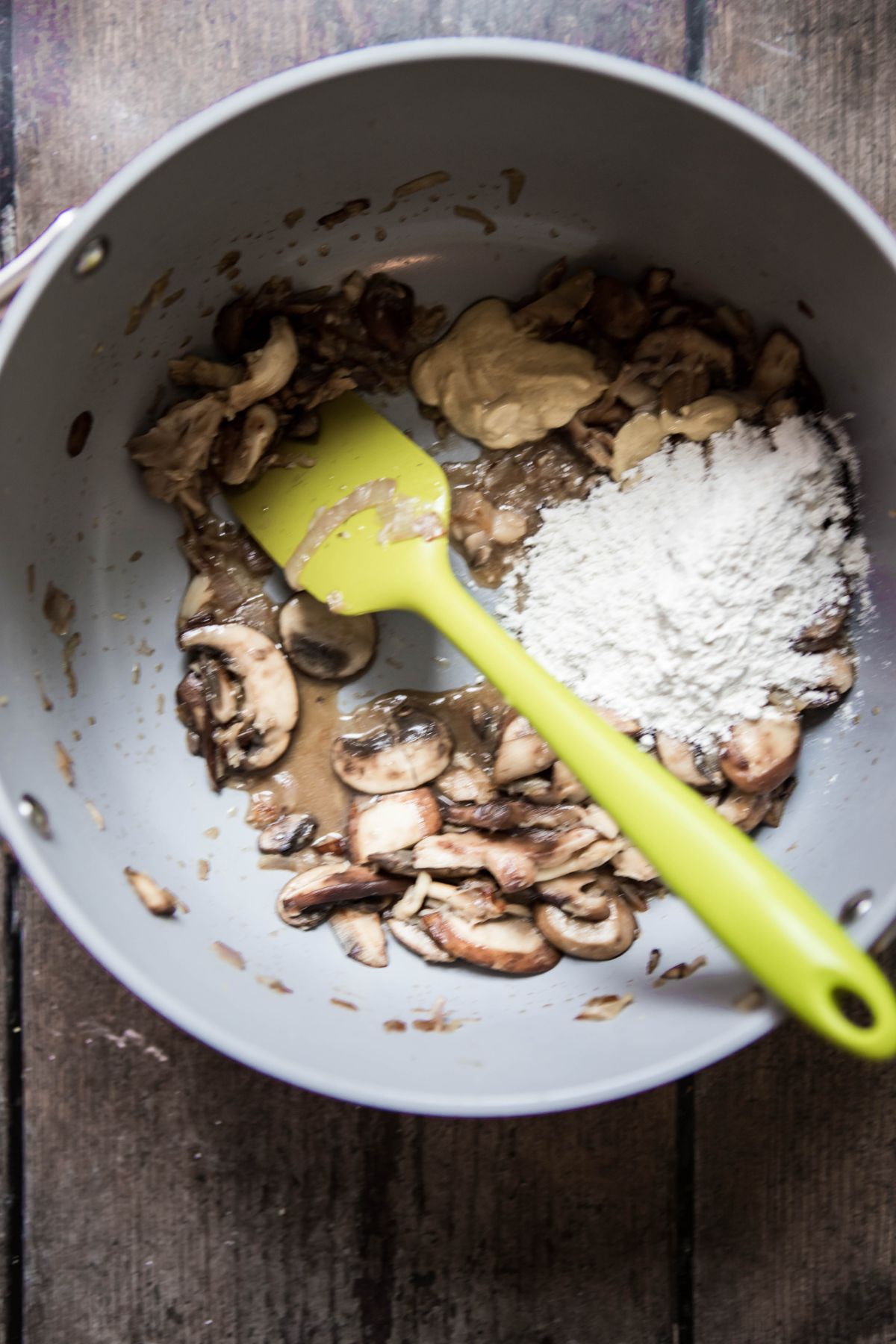 mushrooms with flour and mustard and a green spatula in a pot
