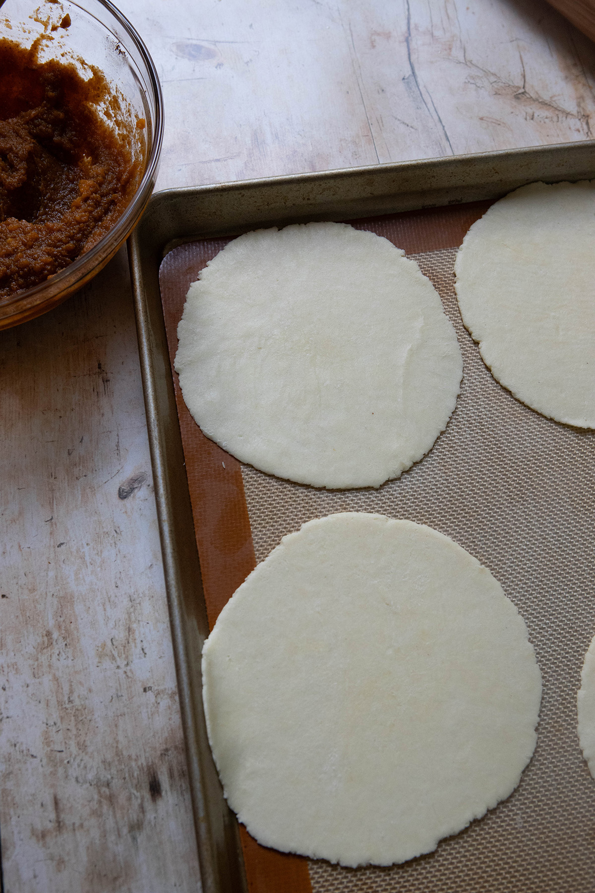 pie dough circles on a baking sheet for pumpkin pasties